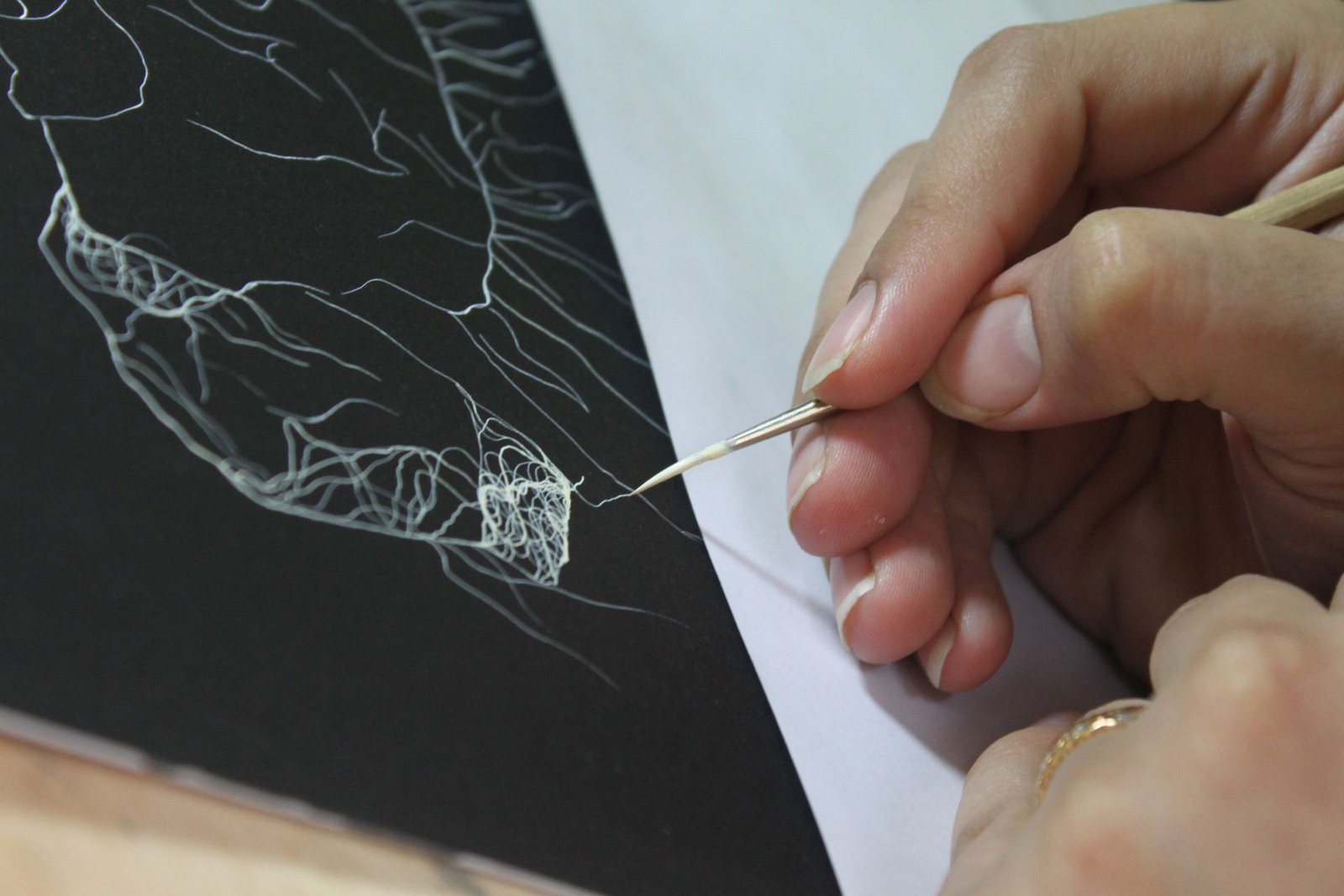 A hand holding a fine brush paints pale thread-like lines on a dark surface